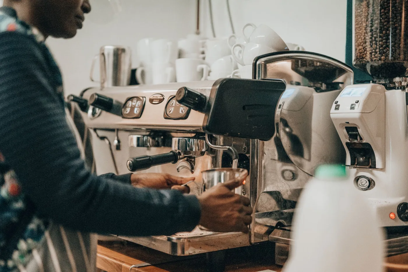 A barista in a striped apron making coffee at an espresso machine